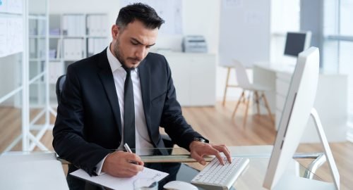 hombre-caucasico-en-traje-de-negocios-sentado-en-la-oficina-trabajando-en-la-computadora-y-escribiendo-en-papel hombre-caucasico-en-traje-de-negocios-sentado-en-la-oficina-trabajando-en-la-computadora-y-escribiendo-en-papel
